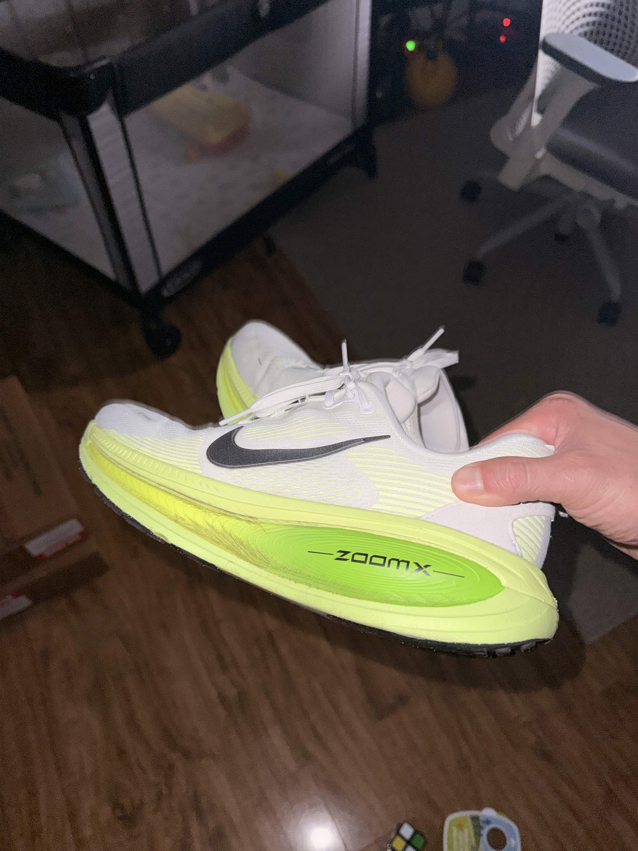 Nike Vomero 18 in white and volt, sitting on the gym floor.