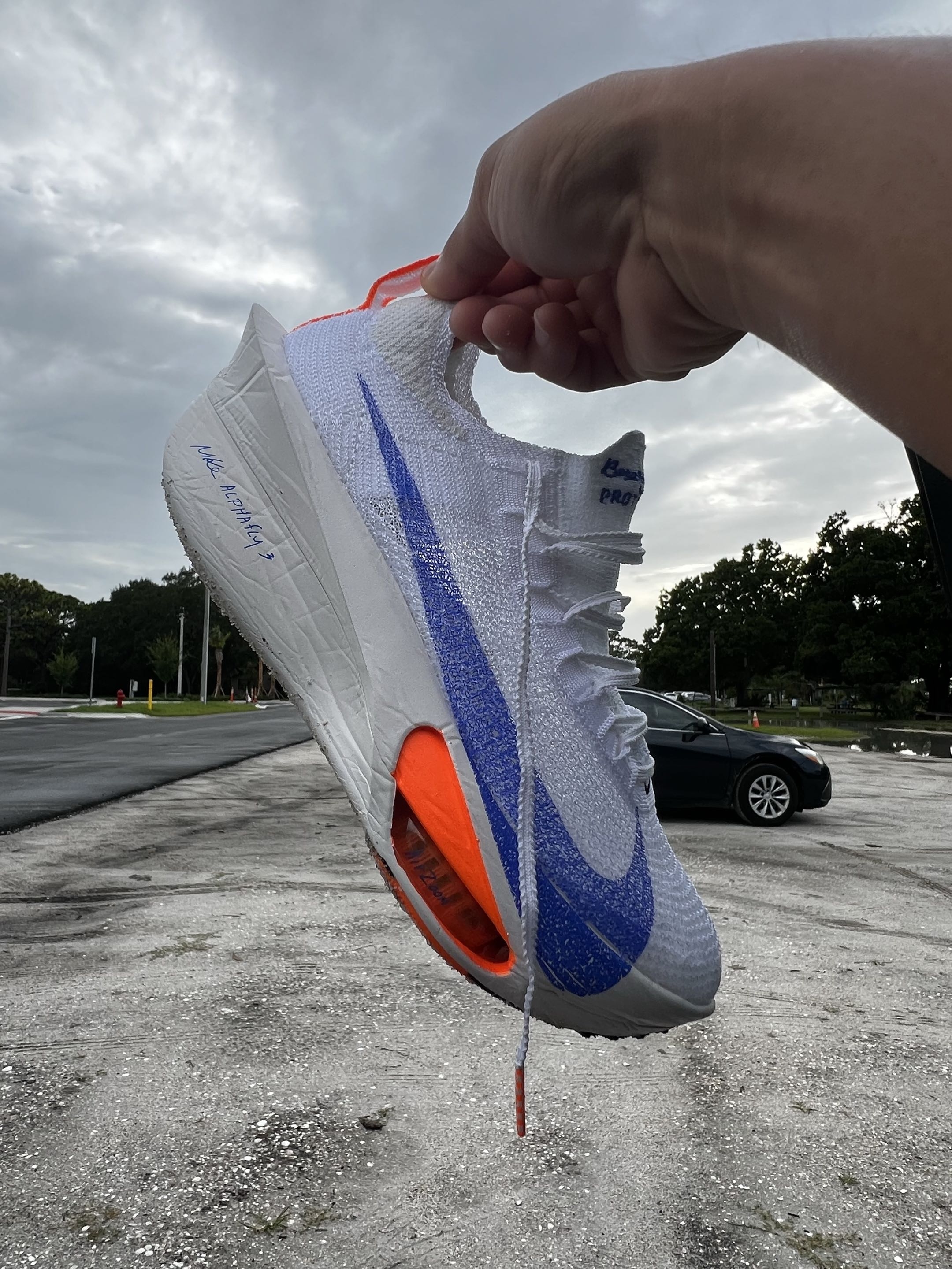 Nike Alphafly 3 in the white/blue Blueprint colorway, held up against an overcast Florida parking-lot sky.