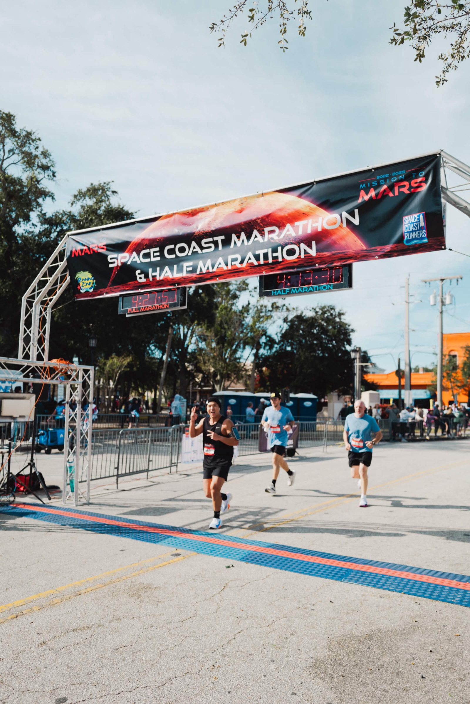 Jae approaching the Spacecoast Marathon finish line in 2024, double peace signs to the camera.